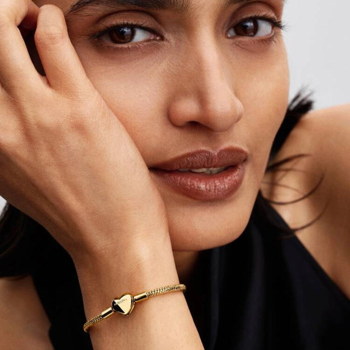 Gold-tone herringbone snake chain bracelet with a polished heart-shaped clasp designed for everyday wear and compatible with charms.