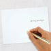 Hand holding a gold pen over a white card with text on a light gray background