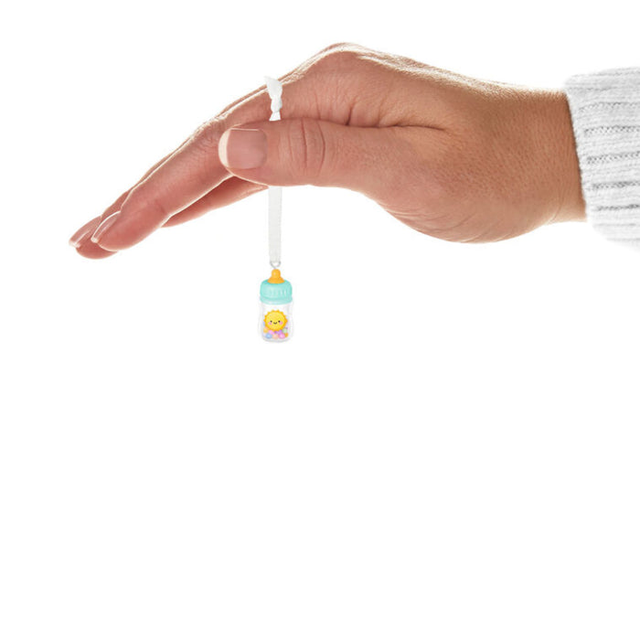 Hand holding a small Decorative baby bottle ornament with a sun design on a white background