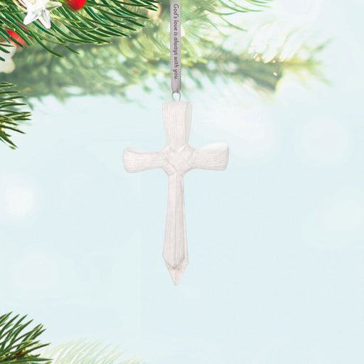 White cross ornament hanging on a Christmas tree 