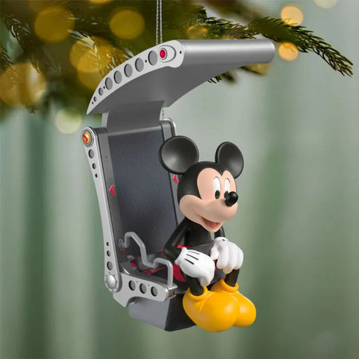 Mickey Mouse hang-glider Christmas ornament hanging from pine branch with golden bokeh holiday lights