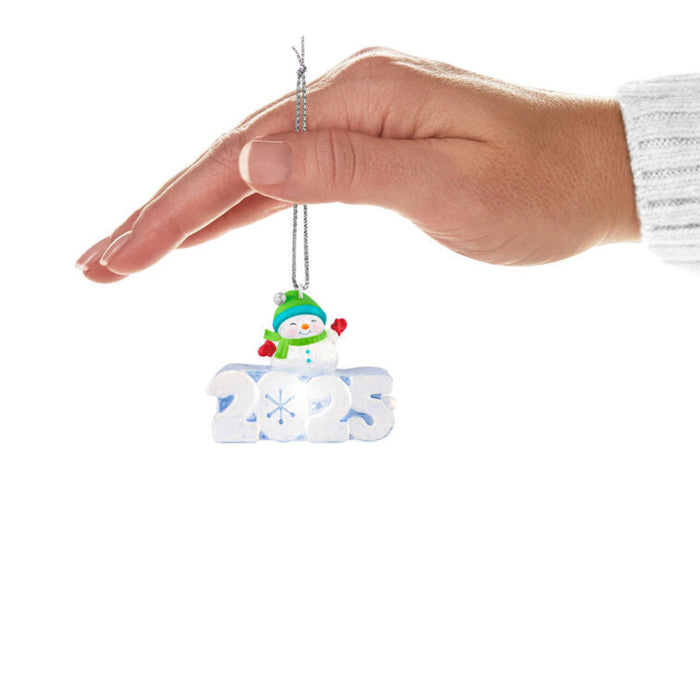 Hand holding a Christmas ornament with a snowman and '2025' on a white background