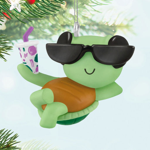 Green sea turtle ornament with sunglasses and a drink, hanging on a Christmas tree.