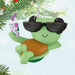 Green sea turtle ornament with sunglasses and a drink, hanging on a Christmas tree.