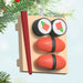 Mini Sushi Ornament with red and red rolls, and black seaweed roll on a wooden board with red chopsticks with light blue and Christmas tree backgreound