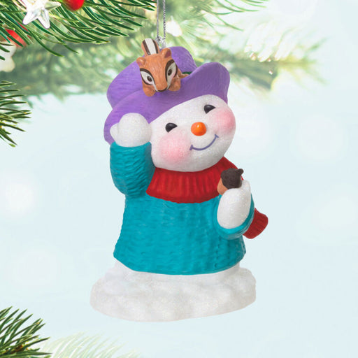 Christmas ornament of a snowman with a purple hat and blue sweater, pointing at his buddy chipmunk , hanging on a Christmas tree