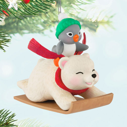 Christmas ornament with a polar bear and penguin on a sleigh, hanging from a tree.