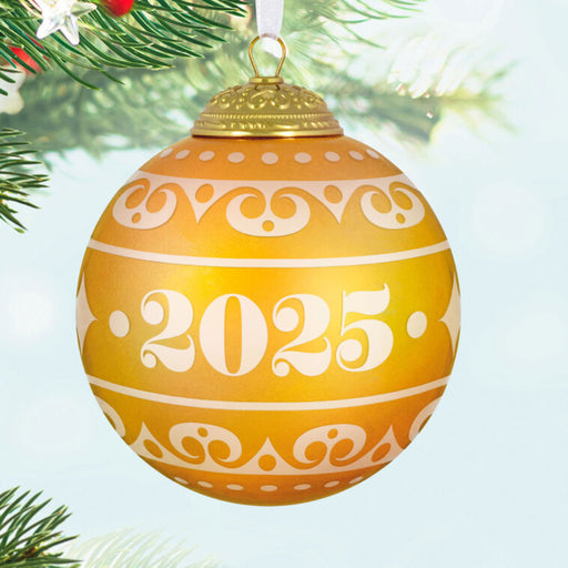 Decorative warm yellow Christmas glass ball ornament with year '2025', on a tree branch