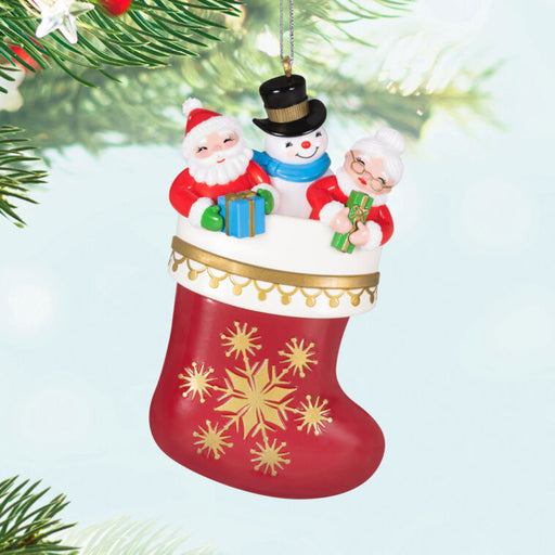 Christmas ornament with Santa, snowman, and woman in a stocking  hanging from a tree. 