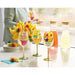 Decorative wine glasses with fruit designs on a table with drinks and fruit.