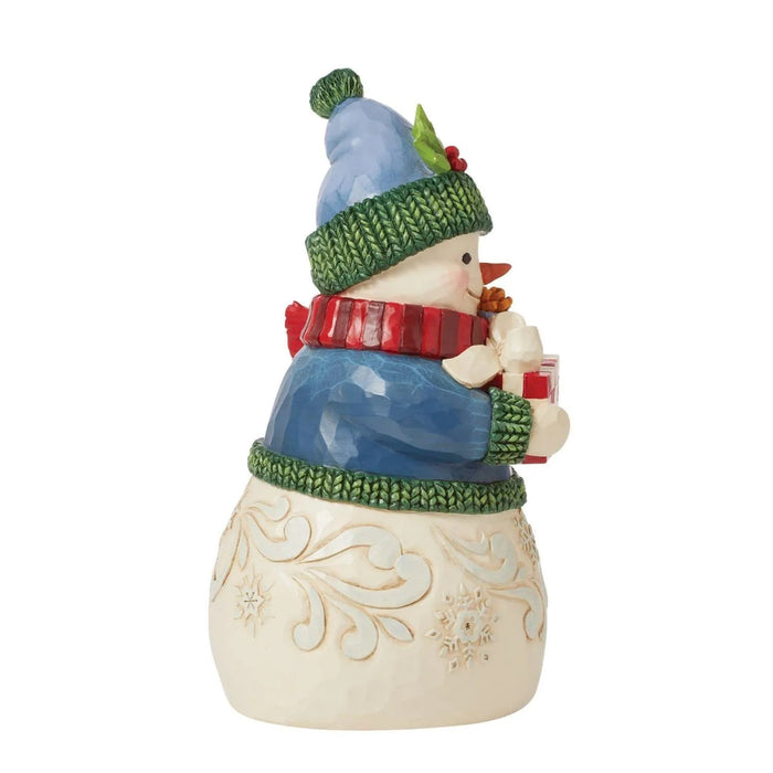 Left side view of Jim Shore Decorative snowman figurine with a blue coat, green hat, and holding presents  on a white background.