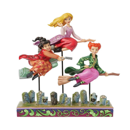 Three Sanderson Sisters  Jim Shore figurines on brooms with a graveyard background base, on a white background 