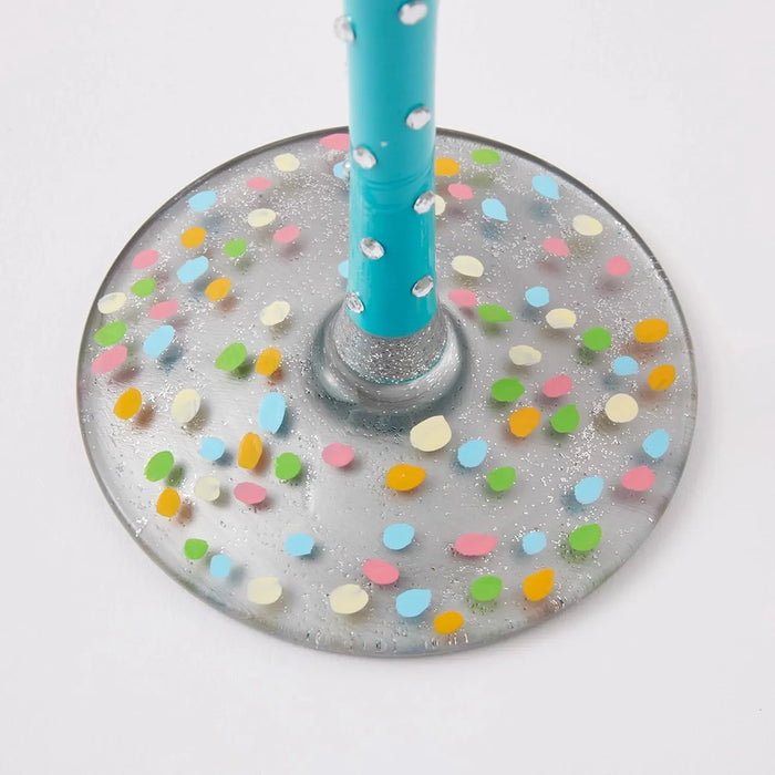 Decorative wine glass base with colorful confetti pattern and a blue straw on a white background