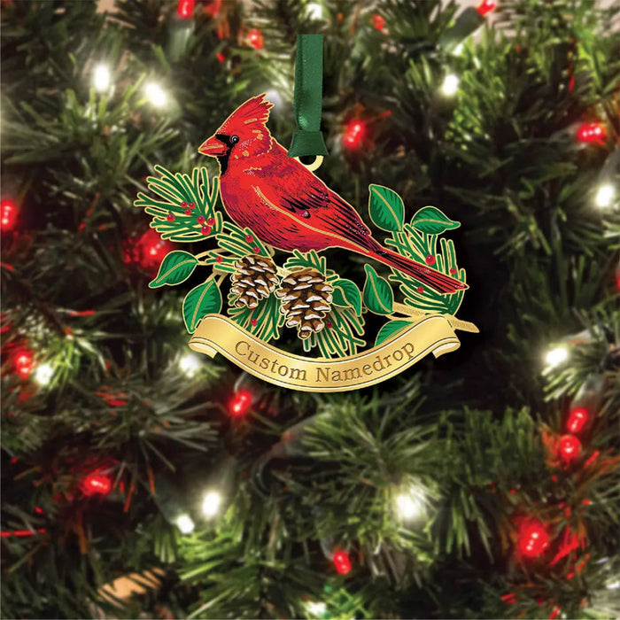 Decorative Christmas ornament with a red cardinal bird on a branch, surrounded by pinecones and leaves, against a Christmas tree background.