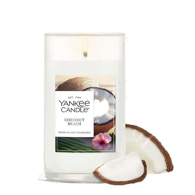 A Yankee Candle coconut beach scented candle in a clear glass jar with a white wax fill, shown with coconut slices on a white background.