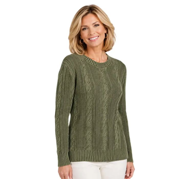A woman wearing an olive green cable-knit crewneck sweater and white pants, standing against a plain white background.