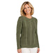 A woman wearing an olive green cable-knit crewneck sweater and white pants, standing against a plain white background.