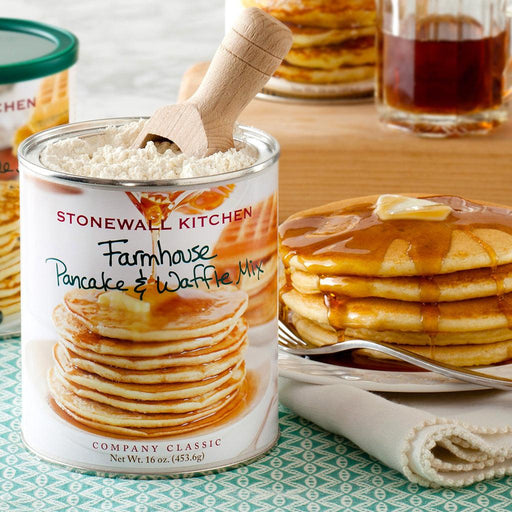 "Stonewall Kitchen Farmhouse Pancake & Waffle Mix in an open 16 oz can with a wooden scoop, placed beside a plate of golden pancakes topped with butter and drizzled with maple syrup, in a cozy breakfast setting."