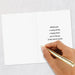 Hand holding a gold pen over a white card with a message on a light gray background
