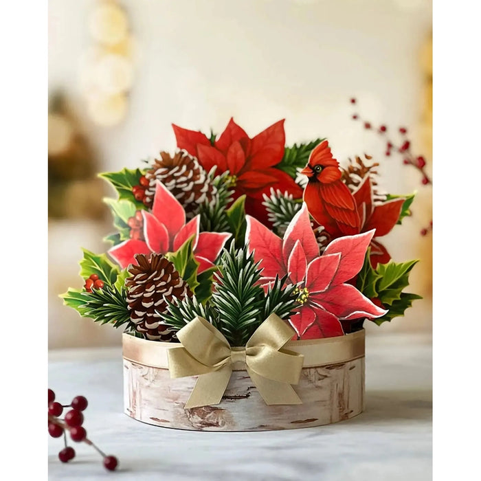 Christmas-themed floral arrangement with poinsettias, pinecones, and a cardinal bird in a decorative pot.