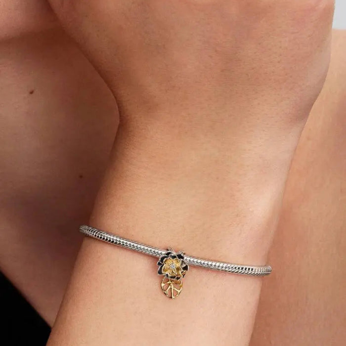 Close‑up of sterling silver and 14k gold‑plated Tiana Water Lily charm on a wrist