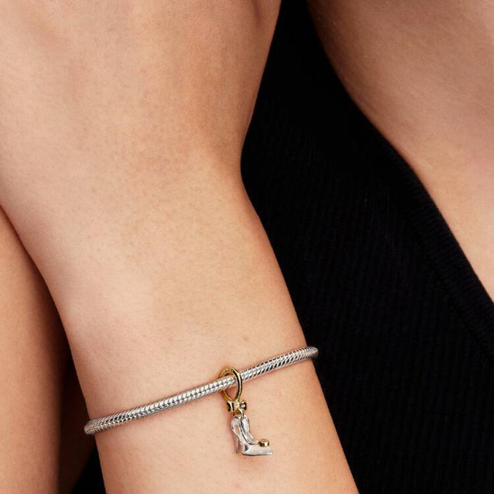 Close‑up of a wrist wearing a charm bracelet featuring the Cinderella slipper charm