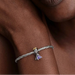 Close-up of a hand wearing a silver bracelet with a charm, against a neutral background.
