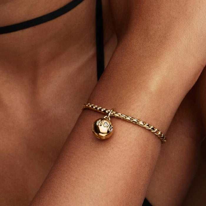 A woman displays a gold bracelet, which includes a small spherical ornament.