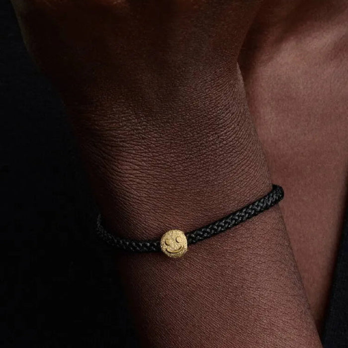 Black braided bracelet with a gold charm on a wrist against a dark background