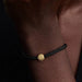 Black braided bracelet with a gold charm on a wrist against a dark background