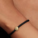 Black braided bracelet with a gold globe charm on a wrist.