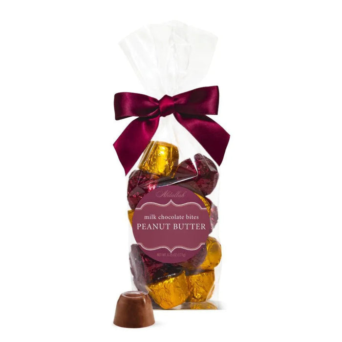 Packaged milk chocolate bites with a peanut butter flavor, tied with a red ribbon on a white background.