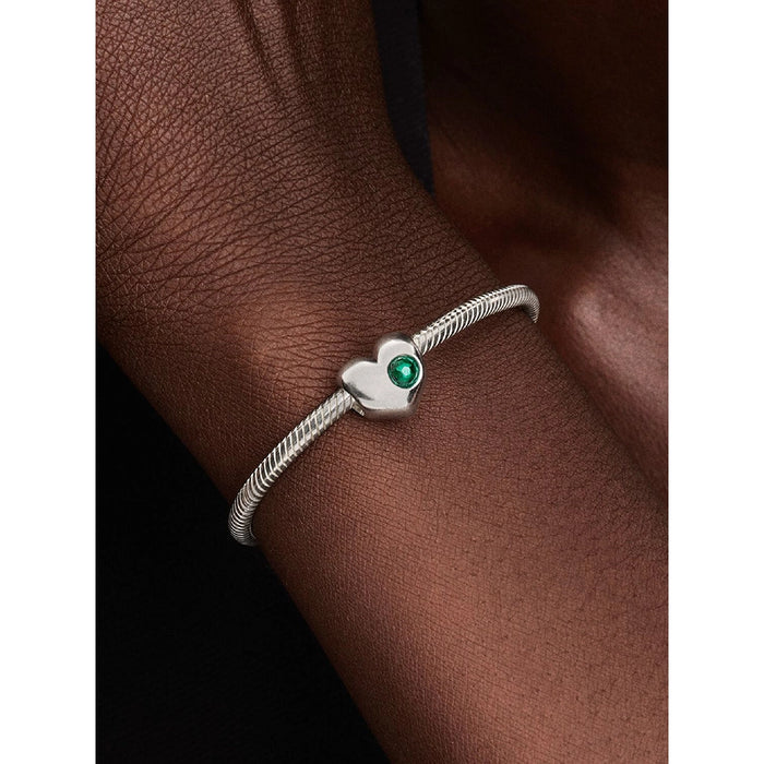 Close-up of a silver Pandora bracelet on a wrist, showcasing the green stone heart charm.