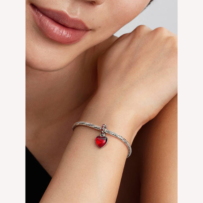 Close-up of a woman's wrist wearing a bracelet with a red heart charm.