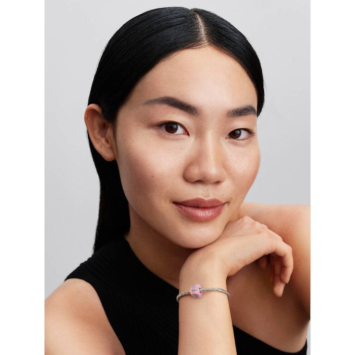 Woman wearing a bracelet with a pink charm on a plain background