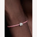 Pink braided bracelet with a silver elephant charm on a wrist 