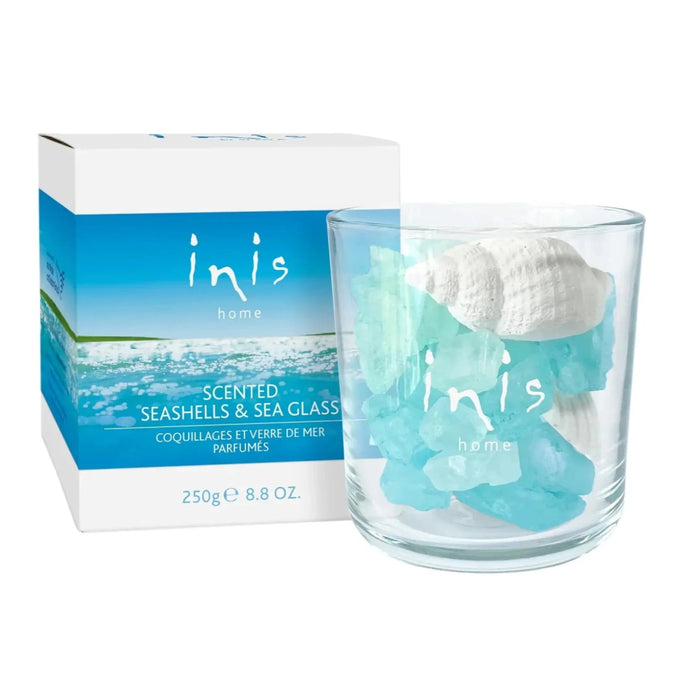 Inis scented seashells and aqua sea glass in a clear glass vessel beside blue and white packaging.