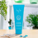 Blue Inis Hair Sea Mineral Conditioner tube (250ml / 8.5 fl. oz.) displayed upright on a wooden table with a soft-focus bathroom setting, starfish accent, and glass stones nearby.