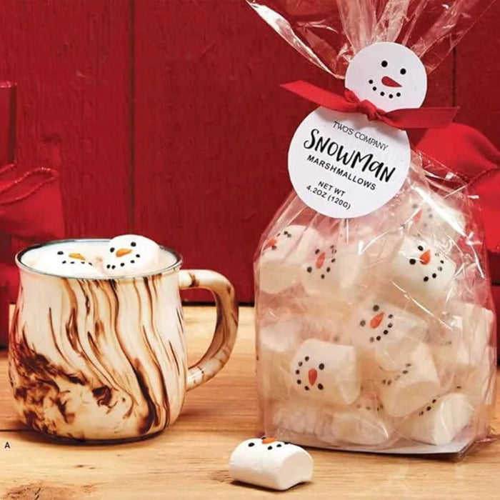Bag of snowman marshmallows with a mug of hot chocolate on a wooden surface.
