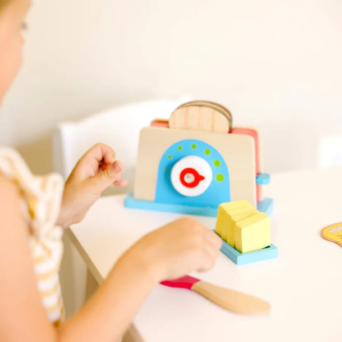 A wooden toy toaster with a knife, a slice of bread, and butter, ideal for creative children's playtime.