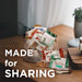 Assorted snack packages on a wooden table with 'Made for Sharing' text.