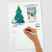 Hand holding a pen over a Christmas-themed card/advent calendar with a tree and cartoon character  from the peanuts gang on a white background.