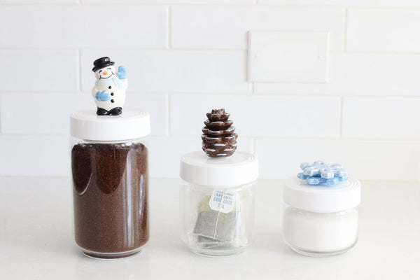 Three glass jars with decorative lids on a white surface.