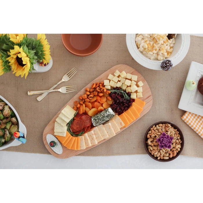 Wooden charcuterie board with assorted meats, cheeses, and fruits on a table with decorative elements.