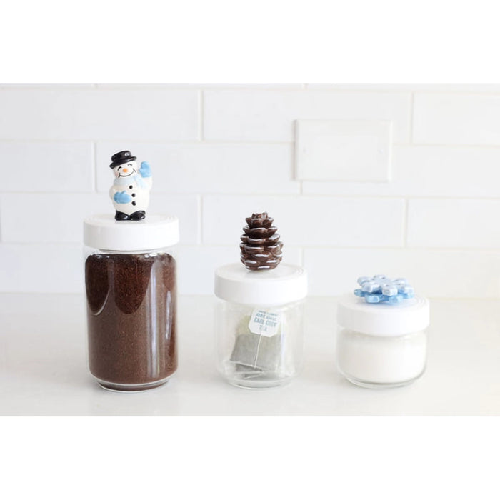 Three glass jars with decorative lids on a white surface