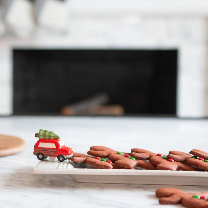 Red toy car with a Christmas tree on a plate of cookies in front of a fireplace.
