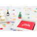 Table setting with a red card, small Christmas tree, and champagne bottle on a polka dot tablecloth.