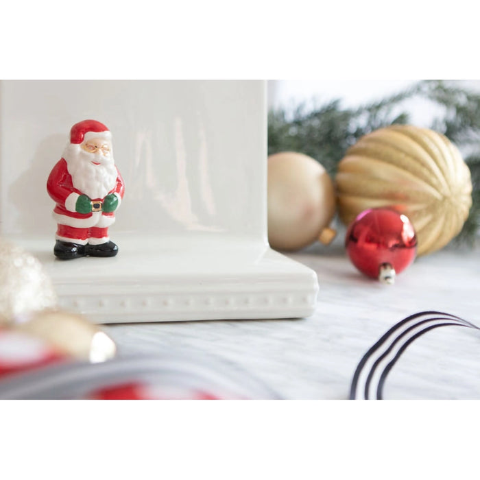 Small Santa Claus figurine on a white surface with Christmas ornaments in the background
