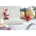 Small Santa Claus figurine on a white surface with Christmas ornaments in the background