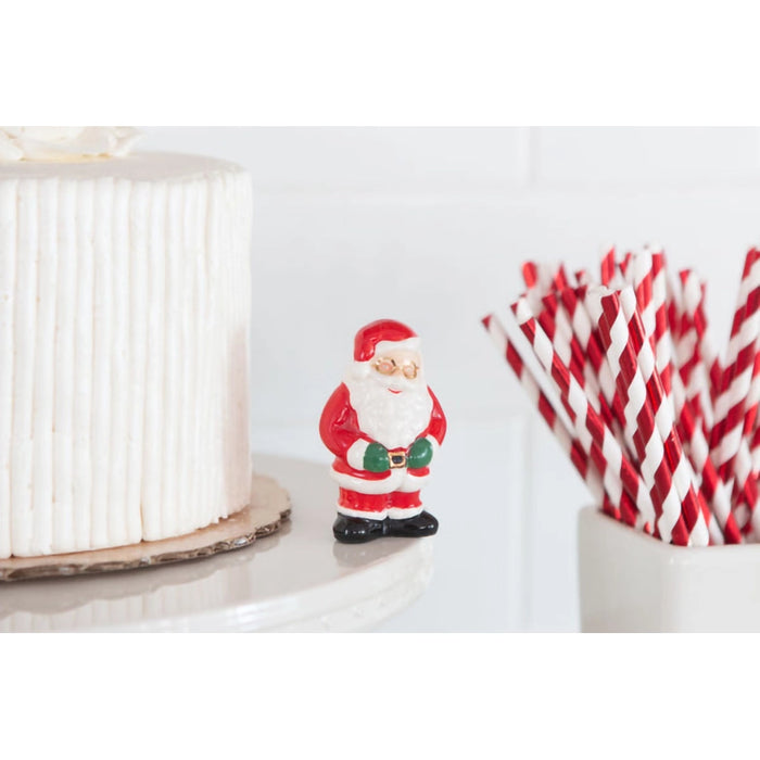 Small Santa Claus figurine next to red and white striped straws on a white surface.